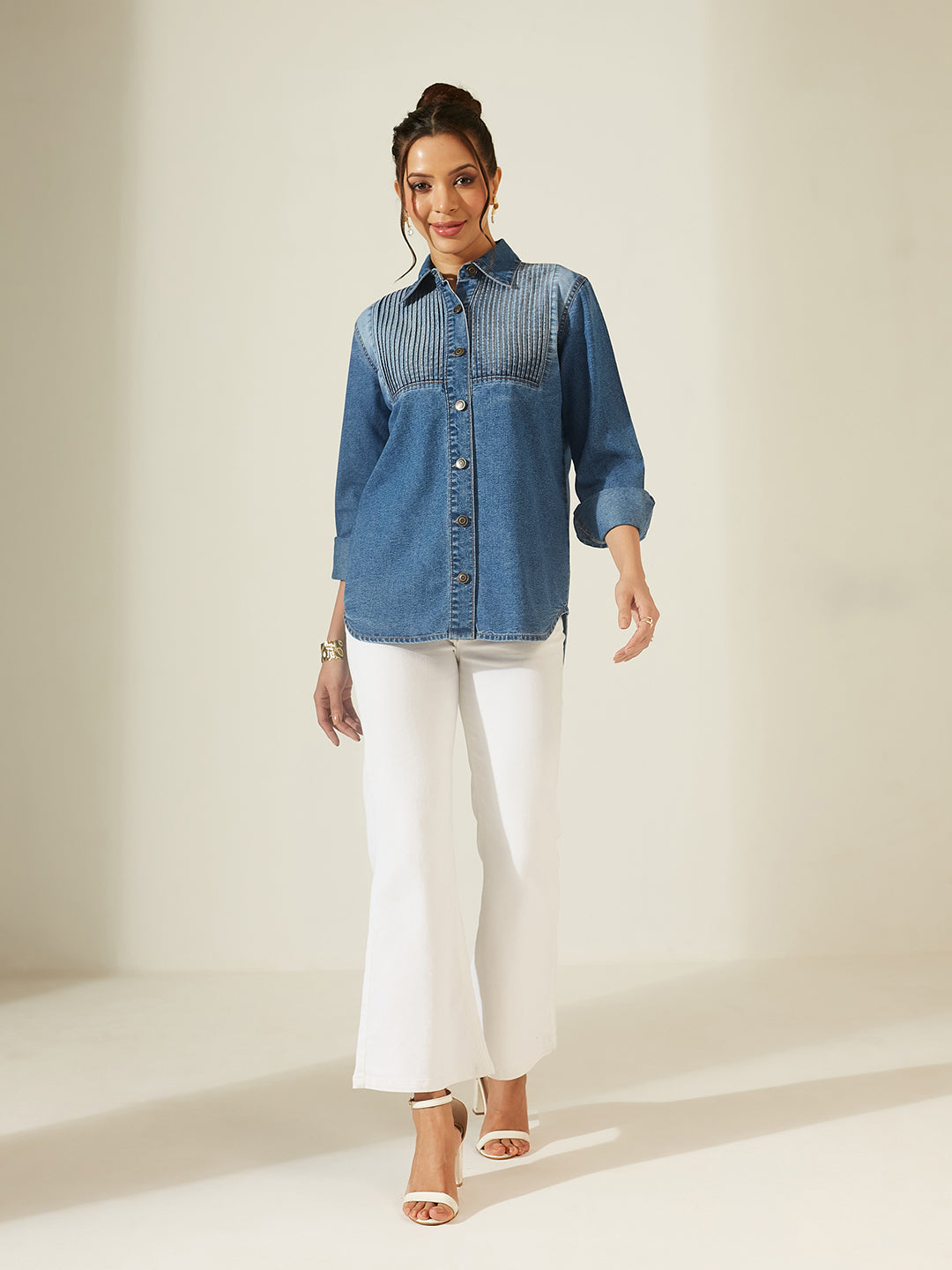 Woman wearing a denim shirt and white pants on a plain background