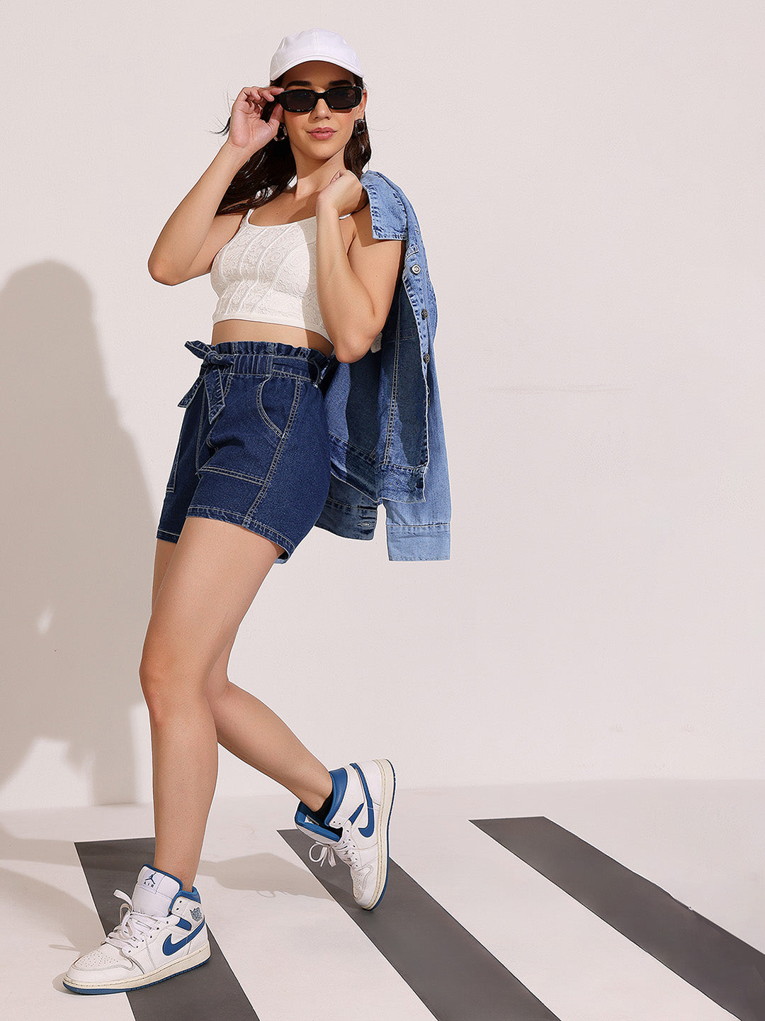 Woman wearing a white crop top, denim shorts, and a denim jacket on a white background
